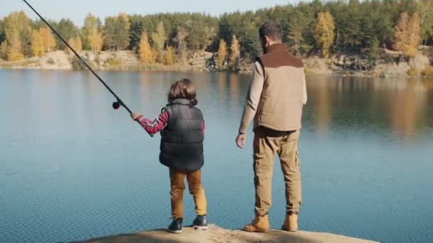 Πίσω όψη του ενήλικου άνδρα και μικρό αγόρι αλιείας στη λίμνη την ηλιόλουστη ημέρα του φθινοπώρου — Αρχείο Βίντεο