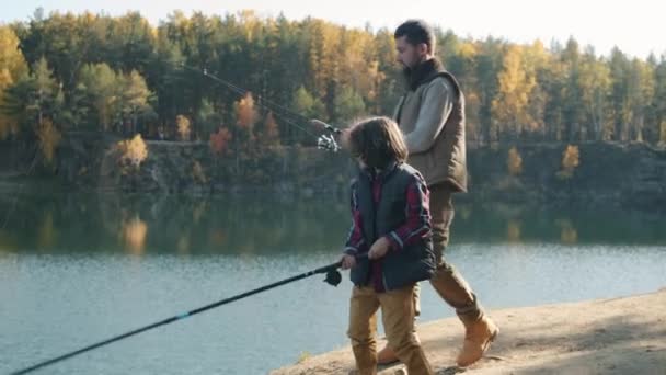 Vater und Sohn fangen am Herbsttag mit Angelruten Fische im Fluss — Stockvideo