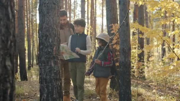 Mujer joven estudiando mapa y hablando con el marido y el hijo en el bosque de otoño — Vídeos de Stock
