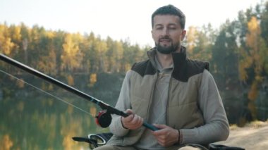 Nehir kıyısında sandalyede oturan neşeli genç balıkçının portresi.