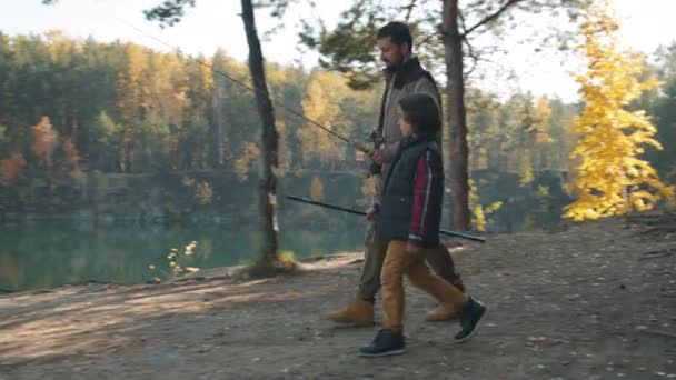 Papa und süßes Kind mit Angelruten spazieren am Herbsttag zum schönen See — Stockvideo