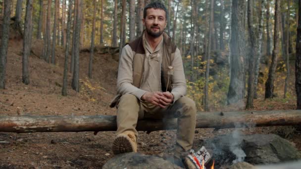 Retrato de turista masculino sentado perto de fogo em bosques segurando marshmallow assado sorrindo — Vídeo de Stock