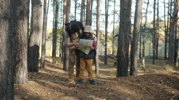 Otec a syn turisté při pohledu na mapu a mluvení stojící v krásném lese — Stock video