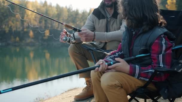 Заботливый отец учит маленького мальчика говорить и рыбачить в озере в прекрасный осенний день — стоковое видео