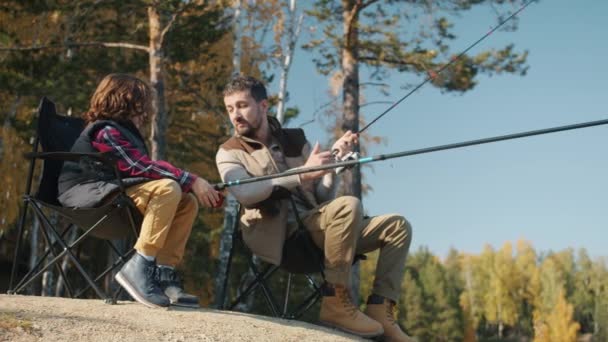 Father and son fishing and talking sitting in chairs on river bank on autumn day — Stock Video