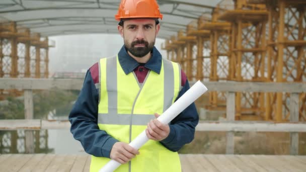 Retrato de un profesional de la construcción parado afuera en el sitio de construcción sosteniendo el plano — Vídeo de stock