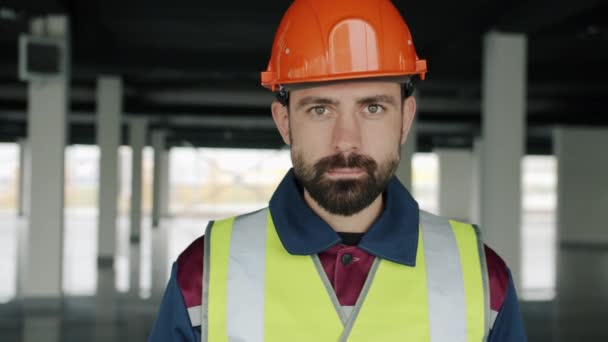 Retrato de profesional en construcción uniforme de pie en interiores con zona de construcción en segundo plano — Vídeo de stock