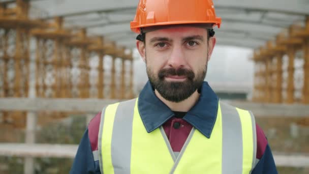 Fröhlicher Bauarbeiter mit Schutzhelm und Weste lächelt im Baustellenbereich — Stockvideo