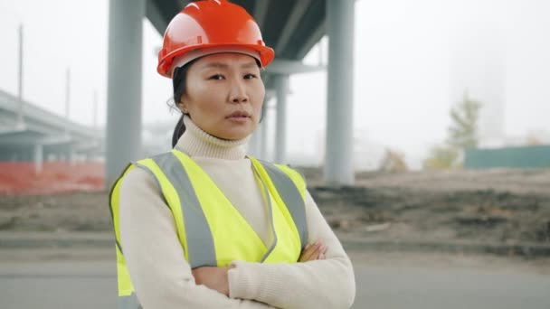 Портрет женщины-инженера-строителя азиатки, стоящей в зоне здания с скрещенными руками — стоковое видео