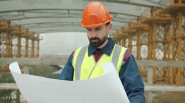 Forma giyen ustabaşının portresi tasarıyı kontrol ediyor ve dışarıda inşaat alanına bakıyor.