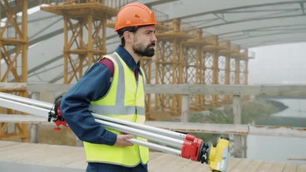 Seitenansicht des Geodäsie-Spezialisten zu Fuß in Baugebiet Ausrüstung tragen Uniform — Stockvideo