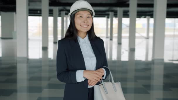 Веселая азиатская бизнесвумен, стоящая в новом коммерческом здании и улыбающаяся — стоковое видео