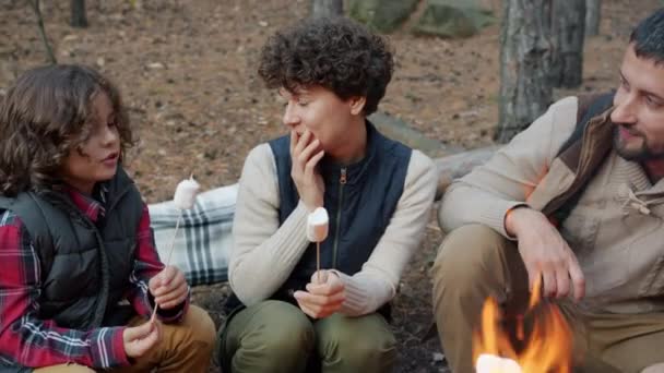 Mamá papá e hijo asando y comiendo malvavisco hablando divirtiéndose alrededor del fuego en el bosque — Vídeo de stock