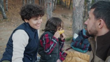 Anne ve baba konuşurken çocuk mısır yiyor ormanda pikniğin tadını çıkarıyor.