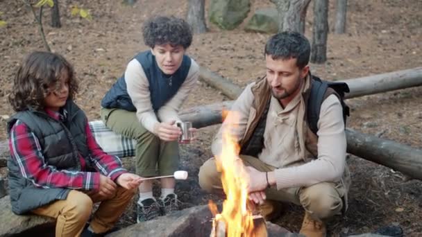 Glückliche Familie kocht Marshmallow am Feuer und genießt das Gespräch — Stockvideo