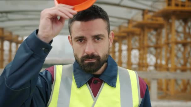 Alegre constructor que se pone el casco de seguridad y sonriendo de pie en el sitio de construcción — Vídeo de stock