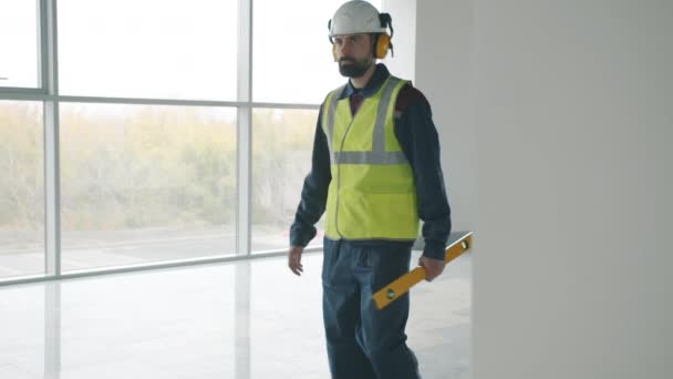 Ouvrier de la construction portant uniforme marchant à l'intérieur du bâtiment industriel tenant l'équipement — Video