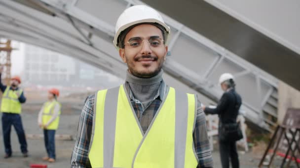 Portret młodego budowniczego Bliskiego Wschodu w mundurze stojącego na placu budowy — Wideo stockowe
