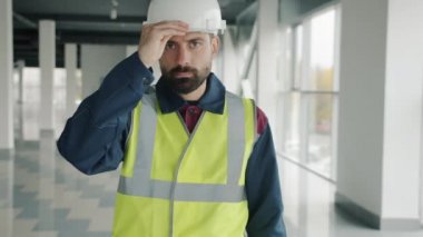 Kask takan ve kollarını çapraz bağlayan genç adamın yavaş çekimde portresi endüstriyel tesiste duruyor.