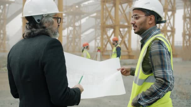 Back view of engineers discussing construction project looking at blueprint — Stock Video