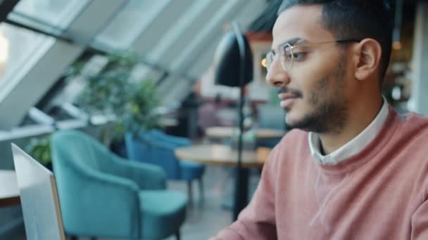 Umkippbares Porträt eines ernsthaften arabischen Mannes, der mit Laptop am Tisch in einem modernen Café sitzt und tippt — Stockvideo