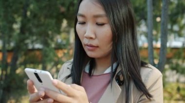Neşeli Asyalı iş kadınının yakın planda akıllı telefon kullanarak ekranda gülümsemesi.