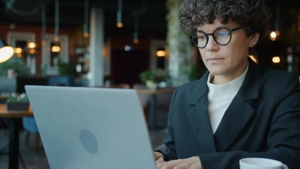 Cámara lenta de la mujer seria que trabaja con el ordenador portátil mirando la escritura de la pantalla en la cafetería — Vídeo de stock