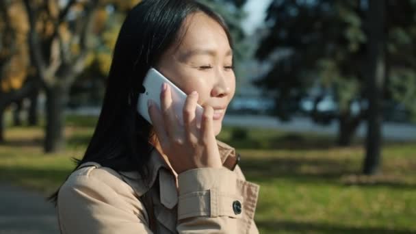 Retrato en cámara lenta del empresario asiático feliz hablando por teléfono móvil y sonriendo afuera en un día soleado — Vídeo de stock