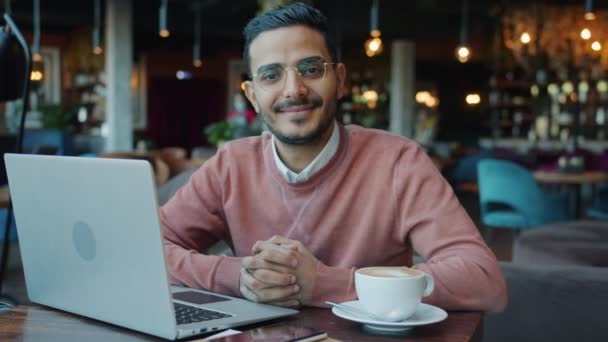Retrato en cámara lenta del guapo chico de Oriente Medio en la cafetería sentado a la mesa con computadora portátil y café — Vídeo de stock