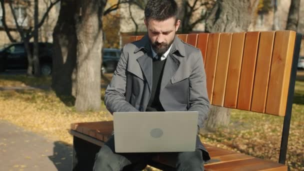 Portret van de ondernemer met behulp van laptop computer buiten zitten op bank alleen typen — Stockvideo