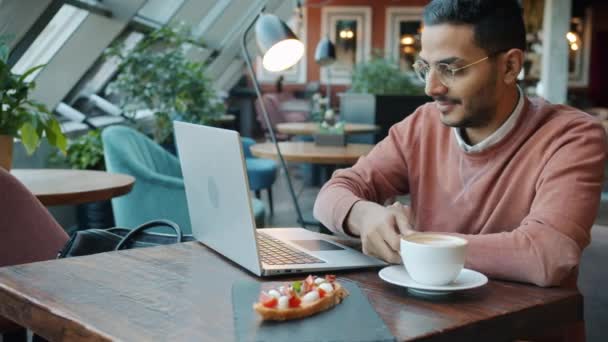 Retrato del estudiante despreocupado usando el ordenador portátil en la cafetería escribiendo sonriendo y tomando café — Vídeo de stock