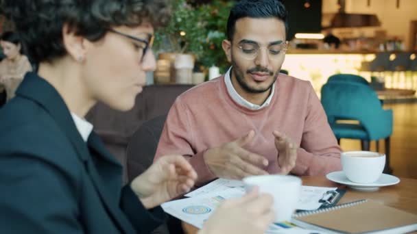 Ближневосточный бизнесмен разговаривает с женщиной-партнером, указывая на бумаги в помещении кафе — стоковое видео