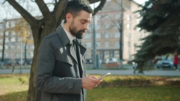 Долли сняла амбициозного парня, гуляющего на улице и пользующегося смартфоном — стоковое видео