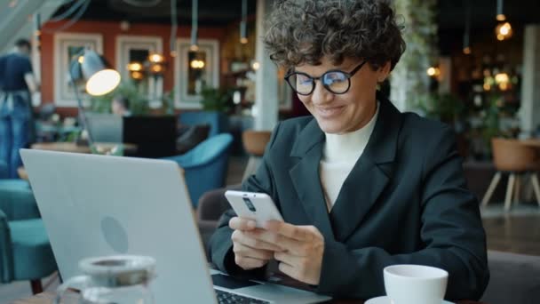 Lykkelig forretningskvinne som bruker smarttelefon-berøringsskjerm med kommunikasjon på nett og sosiale medier på kafe. – stockvideo