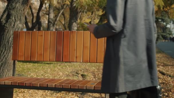 Vážný podnikatel sedí na lavičce a na podzim mluví venku na mobilním telefonu — Stock video