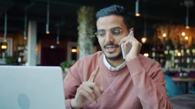 Neşeli Orta Doğulu adam cep telefonuyla konuşuyor ve kafede not defterine notlar yazıyor.