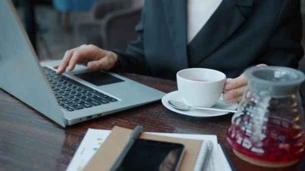 Tilt-up retrato de la mujer de negocios escribiendo con el ordenador portátil y beber café en la cafetería moderna — Vídeo de stock