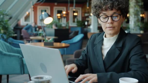 Ambiciosa mujer de negocios utilizando el ordenador portátil y luego responder a la llamada telefónica en la cafetería — Vídeo de stock