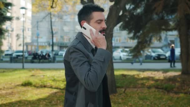 Retrato de un joven en ropa formal caminando fuera en la calle de la ciudad y hablando por teléfono móvil — Vídeo de stock