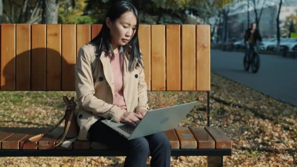 Mladý asijské businesswoman práce s notebook útěk kancelář sedí na lavičce venku — Stock video