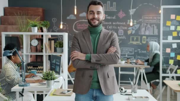 Lassan mozgó portré pozitív fiatal üzletemberről, aki mosolygva áll az irodában. — Stock videók