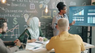 Genç Afrikalı Amerikalı kadın konuşma yapıyor ve ofiste dijital ekran raporları hazırlıyor.