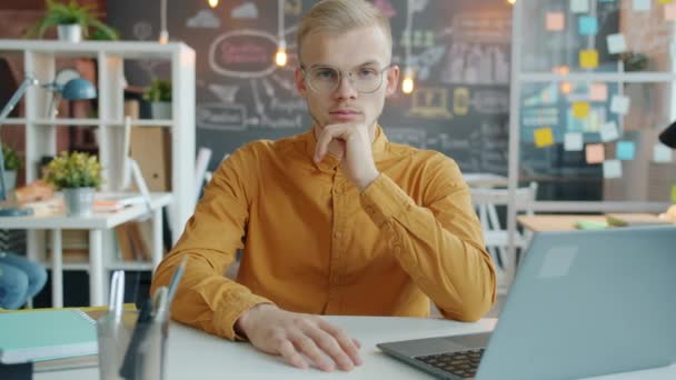 Portrait of successful businessman sitting at computer desk at work while colleague is busy with laptop in background — Stock Video