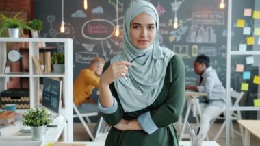 Bağımsız Müslüman girişimcinin yavaş çekim portresi yaratıcı ofiste gözlük tutuyor.