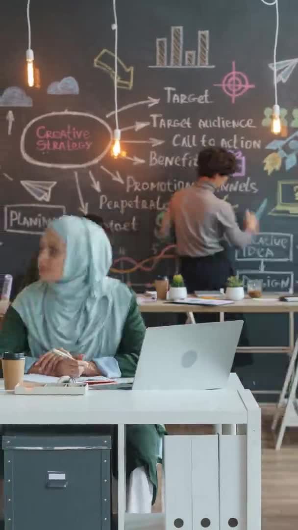 Lapso de tempo de formato vertical de mulher de negócios no hijab usando laptop e colaborando com colegas no escritório compartilhado criativo — Vídeo de Stock