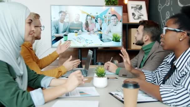Equipo de negocios multiétnicos que tiene videollamada en línea con socios de raza mixta hablando en la oficina — Vídeos de Stock