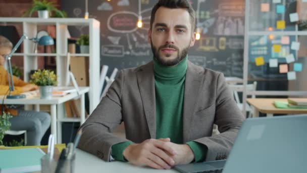 Ritratto di ragazzo attraente seduto alla scrivania in un luogo di lavoro creativo mentre collega utilizzando il computer in background — Video Stock