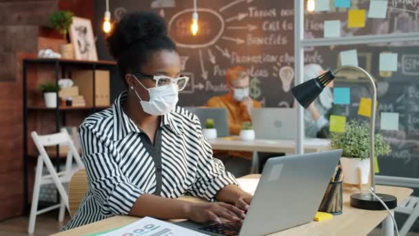 사무실에서 일하는 랩탑을 사용하여 의료용 마스크를 쓰고 있는 아프리카 계 미국인 사업가 — 비디오