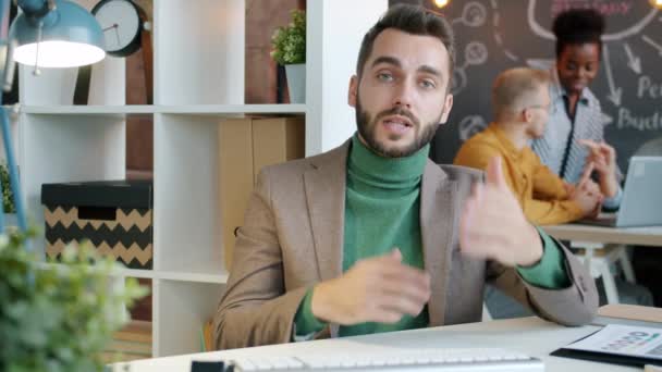 Красивий хлопець офіс працівник розмовляє за столом під час відеодзвінка з робочого місця — стокове відео