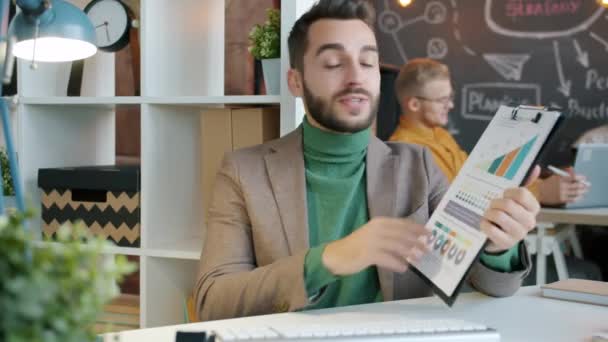 Glada kille talar om affärsframgångar och pekar på diagram under videosamtal på kontoret — Stockvideo
